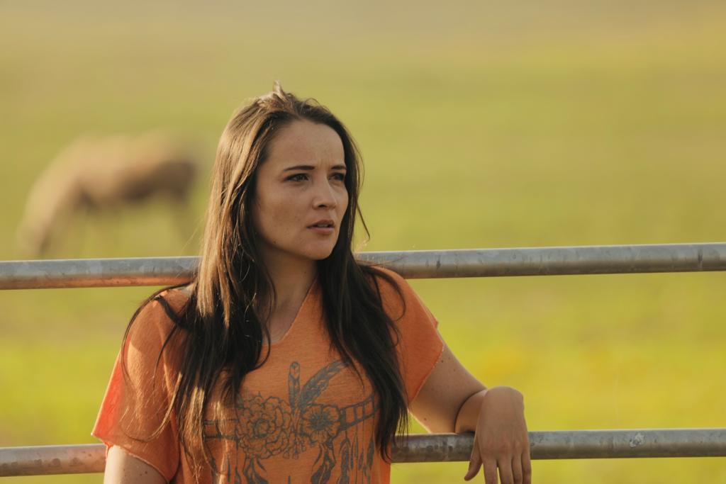 femme adossée sur une barrière dans un ranch
